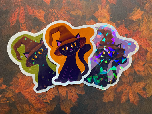 Three black cat stickers with different backgrounds and finishes. Green background with stars, orange background with clear, and purple background with shards.